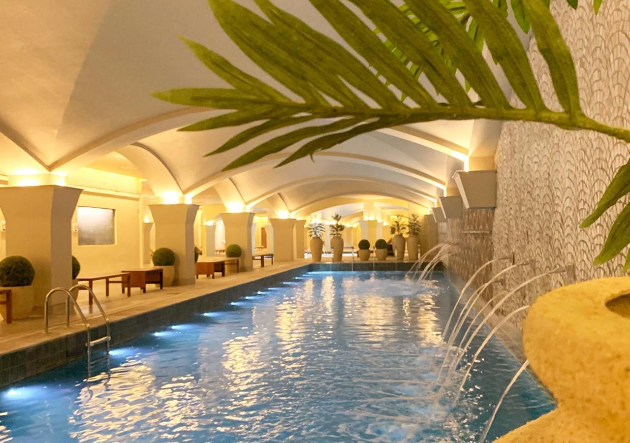 Buona Vitta Gramado Resort & Spa By Gramado Parks Екстериор снимка The photo shows an indoor swimming pool with a serene and elegant atmosphere. The pool has a calm blue water surface, illuminated by soft lights along its edges. The architectural design features arches in the ceiling, creating an open and spacious f