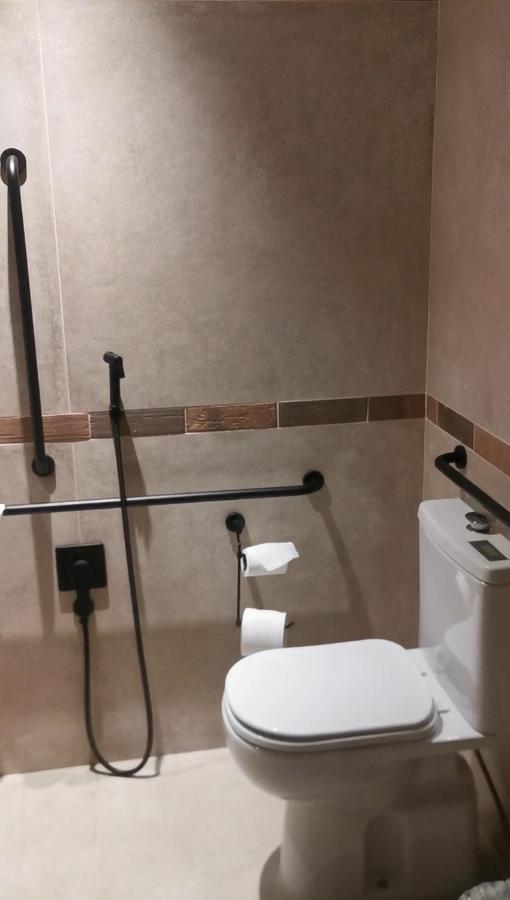 Buona Vitta Gramado Resort & Spa By Gramado Parks Екстериор снимка The photo shows a bathroom equipped with grab bars for accessibility. The walls are tiled in a neutral color, and there is a toilet on the right side of the image. Two rolls of toilet paper are positioned near the toilet, and there are additional ins
