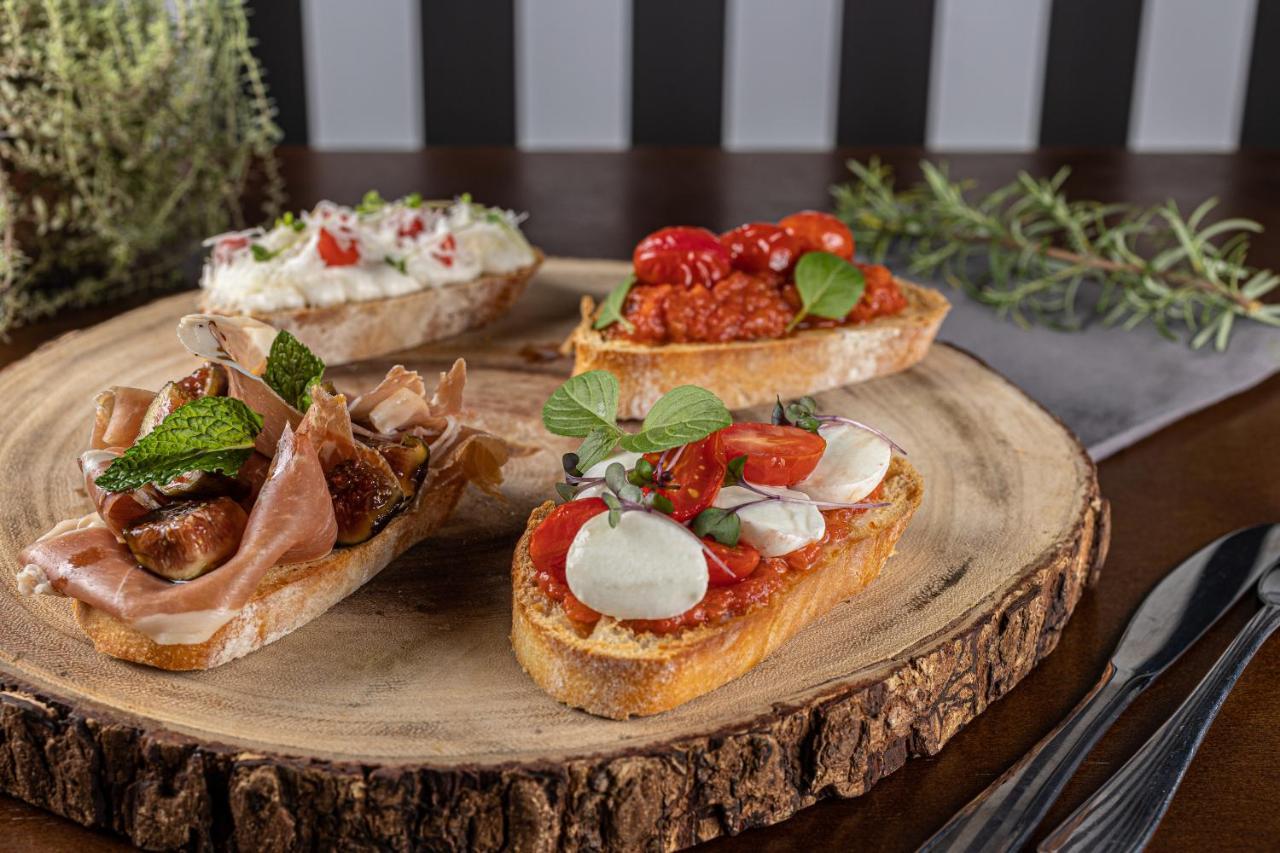 Buona Vitta Gramado Resort & Spa By Gramado Parks Екстериор снимка The photo displays a wooden serving platter featuring four different types of bruschetta. Each piece of bruschetta is topped with various ingredients:

1. The top left has a creamy spread, possibly cheese or ricotta, garnished with fresh herbs and sm