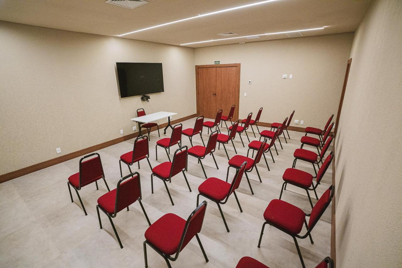 Buona Vitta Gramado Resort & Spa By Gramado Parks Екстериор снимка The photo shows a conference or meeting room with a simple and modern design. There are several rows of red chairs arranged in a semi-circle facing a white table at the front. On the wall opposite the chairs, there is a flat-screen television mounted