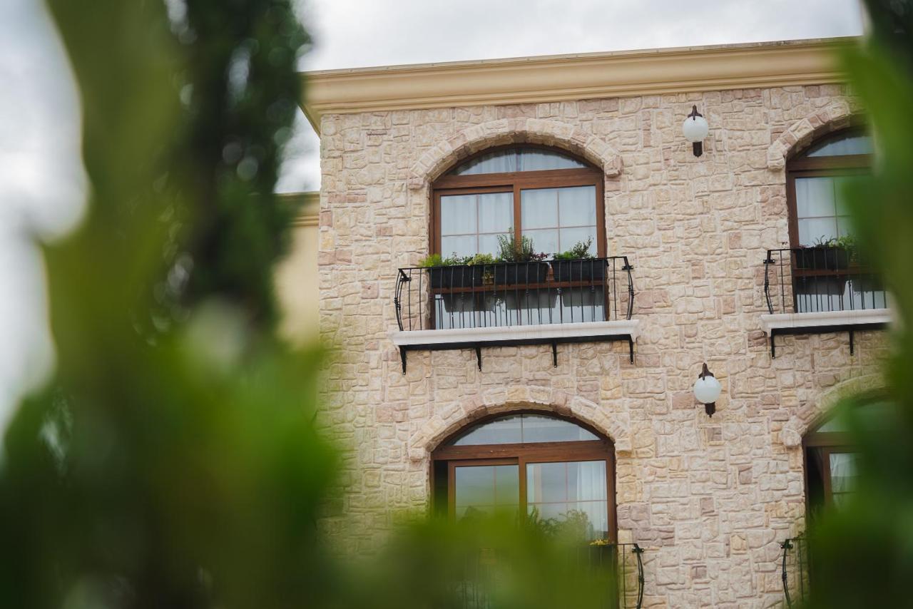 Buona Vitta Gramado Resort & Spa By Gramado Parks Екстериор снимка The photo depicts a stone building with a textured exterior. It features several windows with wooden frames. Each window has a small balcony adorned with decorative plants. There are also wall-mounted light fixtures flanking the windows. In the foreg