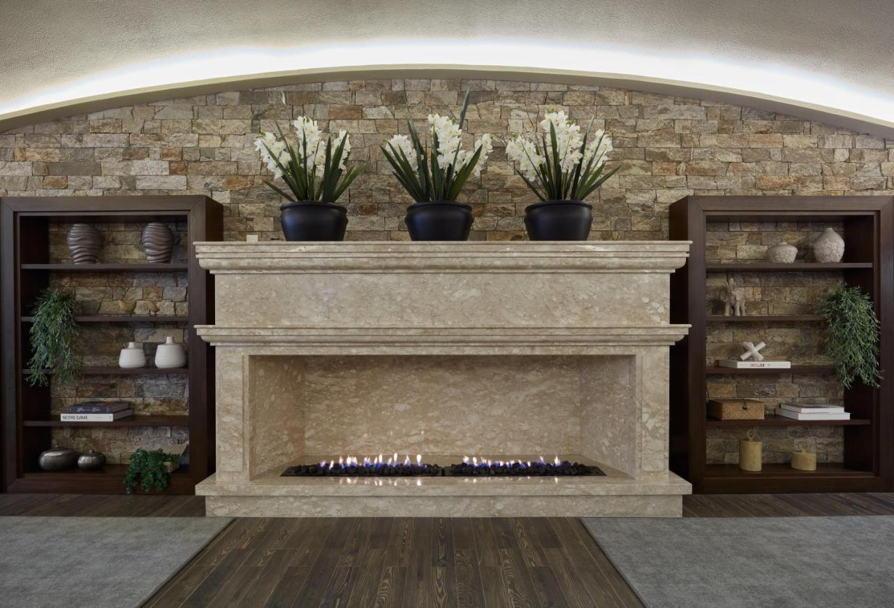 Buona Vitta Gramado Resort & Spa By Gramado Parks Екстериор снимка The photo shows a modern fireplace design built into a wall with a textured stone background. The fireplace is made of a light-colored stone and features a long, narrow gas flame visible at the bottom. Above the fireplace, there are two large potted 