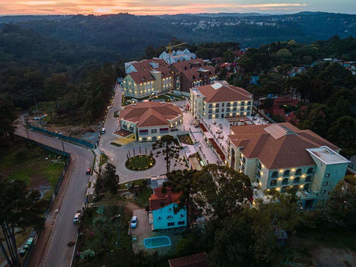 Buona Vitta Gramado Resort & Spa By Gramado Parks Екстериор снимка The photo shows an aerial view of a hotel complex set in a hilly, wooded area. The buildings feature a mix of architectural styles with several structures, including a central round pavilion. Surrounding the buildings are well-maintained gardens and 