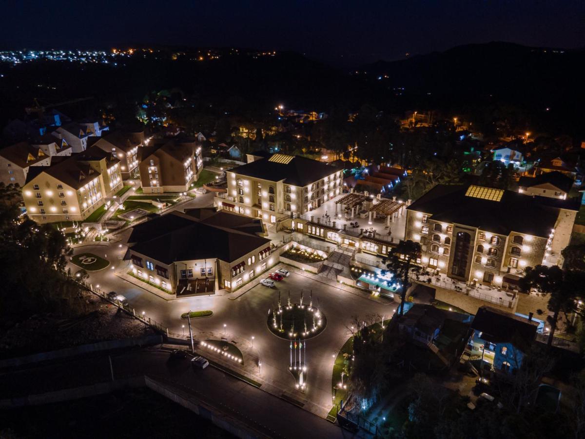 Buona Vitta Gramado Resort & Spa By Gramado Parks Екстериор снимка The photo shows a beautifully lit resort or hotel complex taken at night. The buildings are well-illuminated, highlighting their architecture. There is a circular area with a fountain at the center, surrounded by pathways that connect various parts o