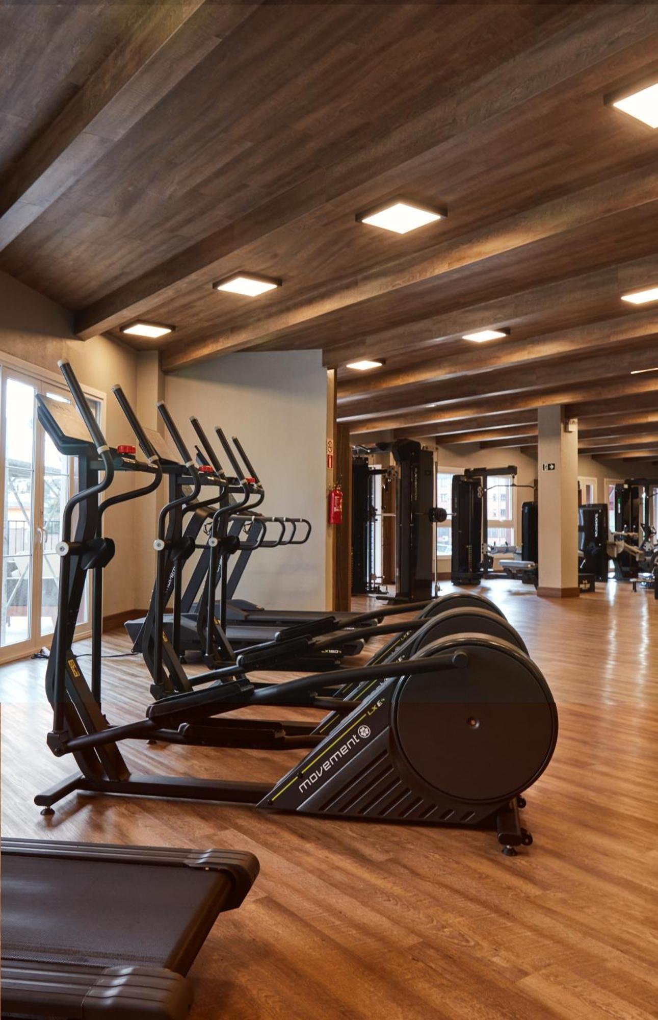 Buona Vitta Gramado Resort & Spa By Gramado Parks Екстериор снимка The photo shows a modern gym interior with wooden flooring and a ceiling with wooden beams. There are several exercise machines, including elliptical trainers and a treadmill, positioned in the foreground. In the background, there are additional work