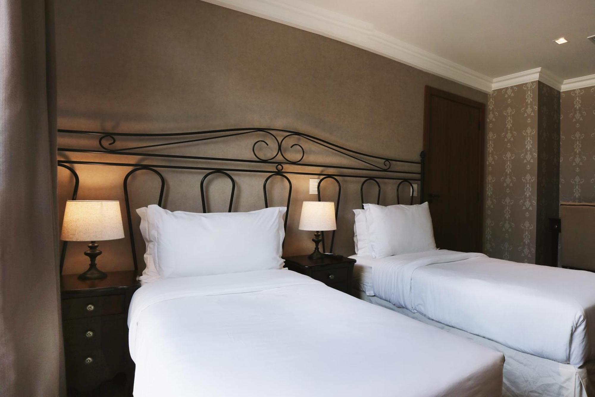 Buona Vitta Gramado Resort & Spa By Gramado Parks Екстериор снимка The photo shows a neatly arranged hotel room featuring two single beds with white bedding. The beds have decorative metal headboards, and there are bedside tables on either side with lamps. The room's walls have a subtle design, and there is a door v
