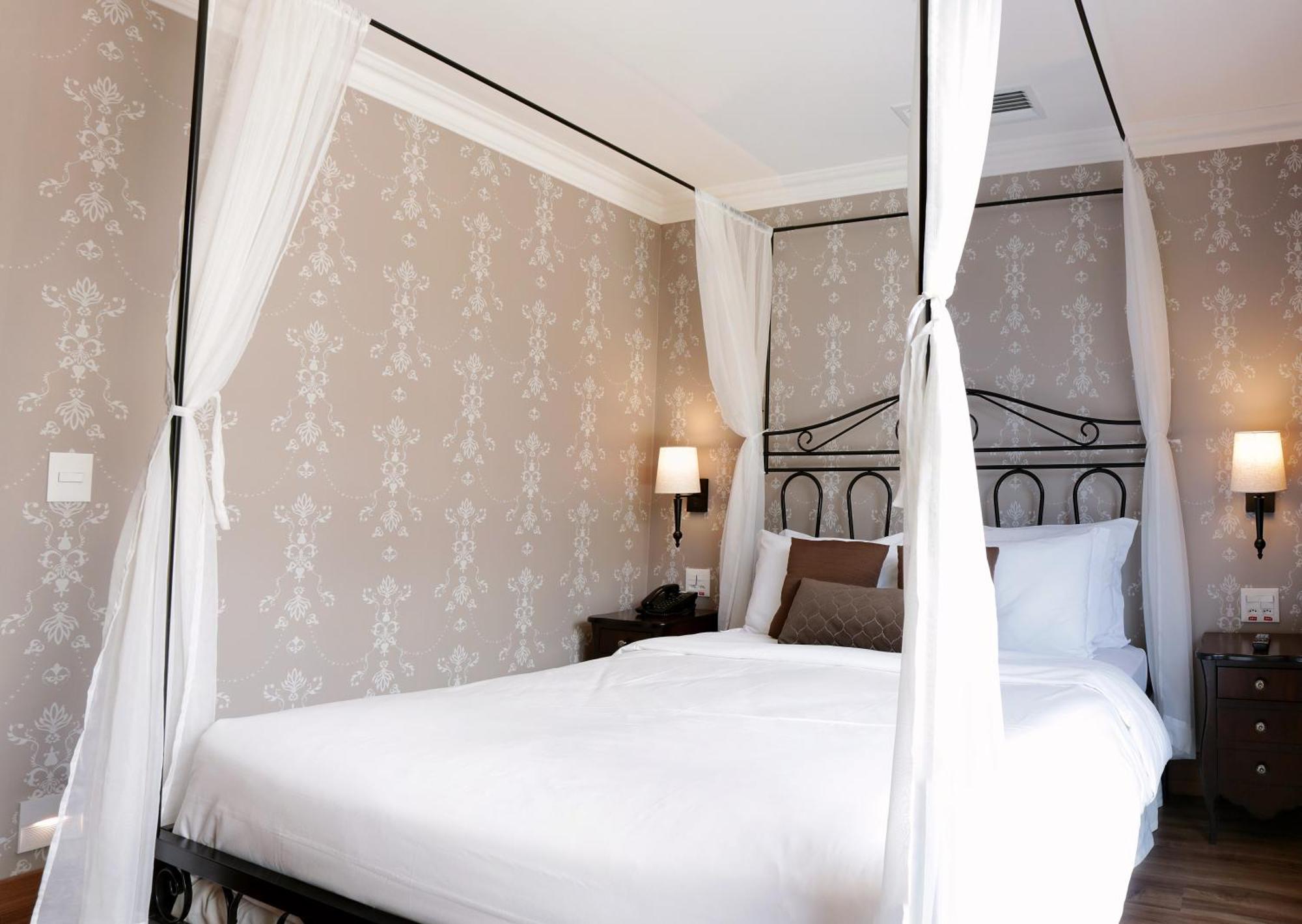 Buona Vitta Gramado Resort & Spa By Gramado Parks Екстериор снимка The photo shows a elegantly decorated bedroom featuring a four-poster bed with white drapes. The bed is made with white linens and has some brown accent pillows. The walls are adorned with a subtle floral pattern, and there are two bedside lamps prov