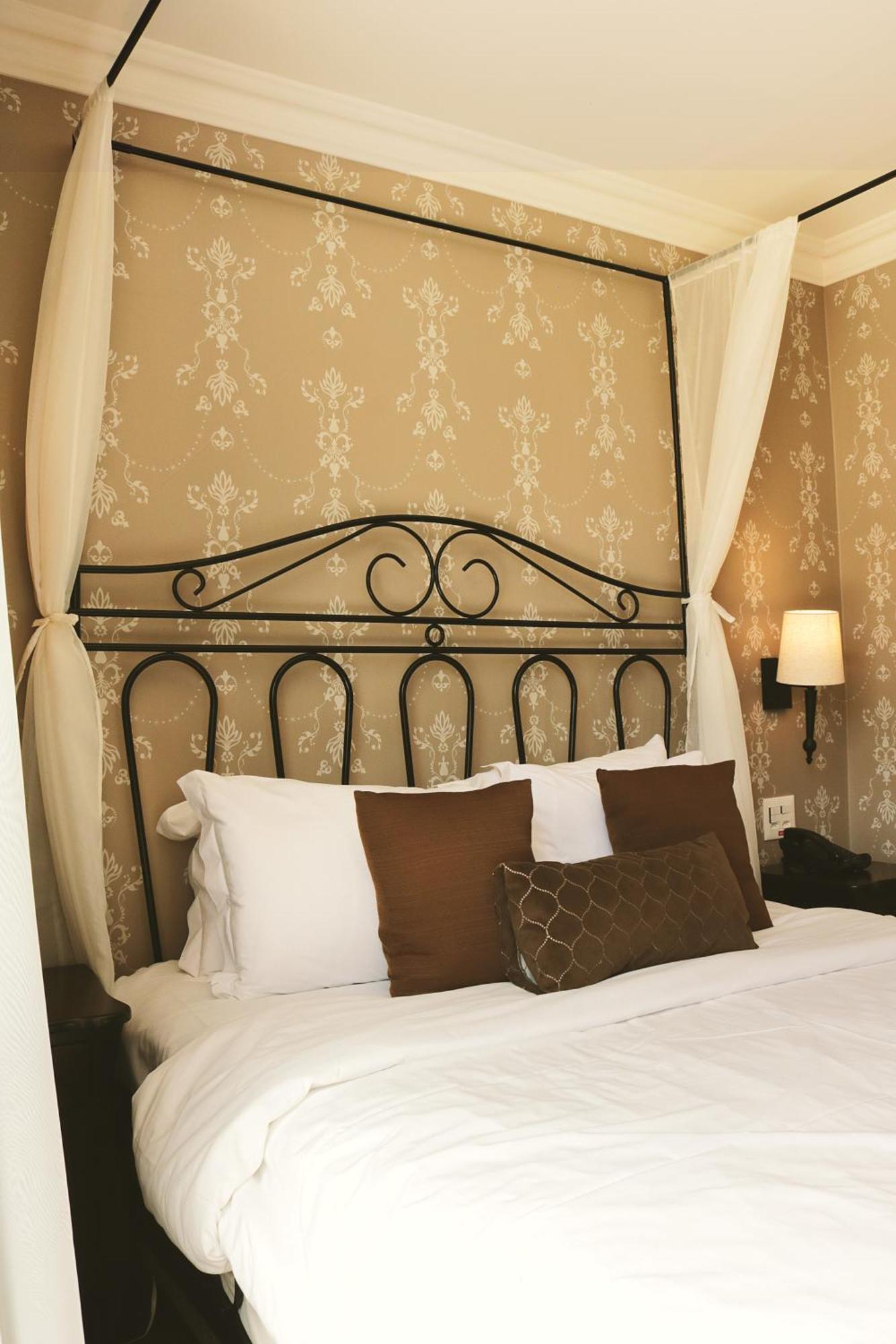 Buona Vitta Gramado Resort & Spa By Gramado Parks Екстериор снимка The photo shows a cozy bedroom setup featuring a decorative metal bed frame with a scroll design as the headboard. The bed is adorned with several white pillows and two brown decorative cushions. The wall behind the bed is covered with a light-colore