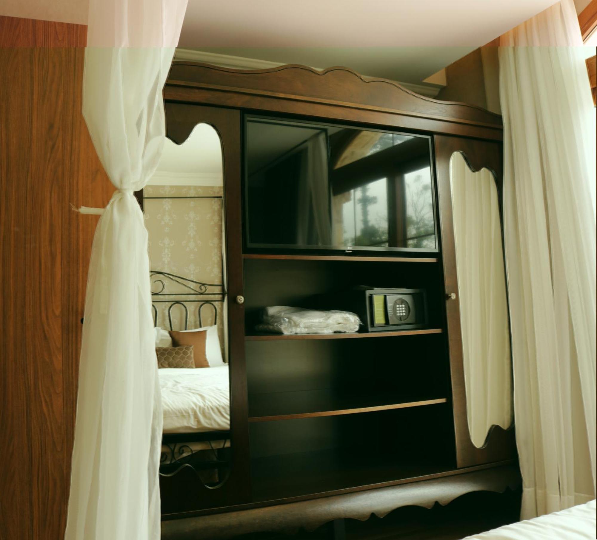 Buona Vitta Gramado Resort & Spa By Gramado Parks Екстериор снимка The image shows a wooden cabinet with a television mounted on the front. The cabinet has decorative edges and is paired with sheer white curtains on either side. Inside the cabinet, there are shelves, and a small safe or storage box is visible on one