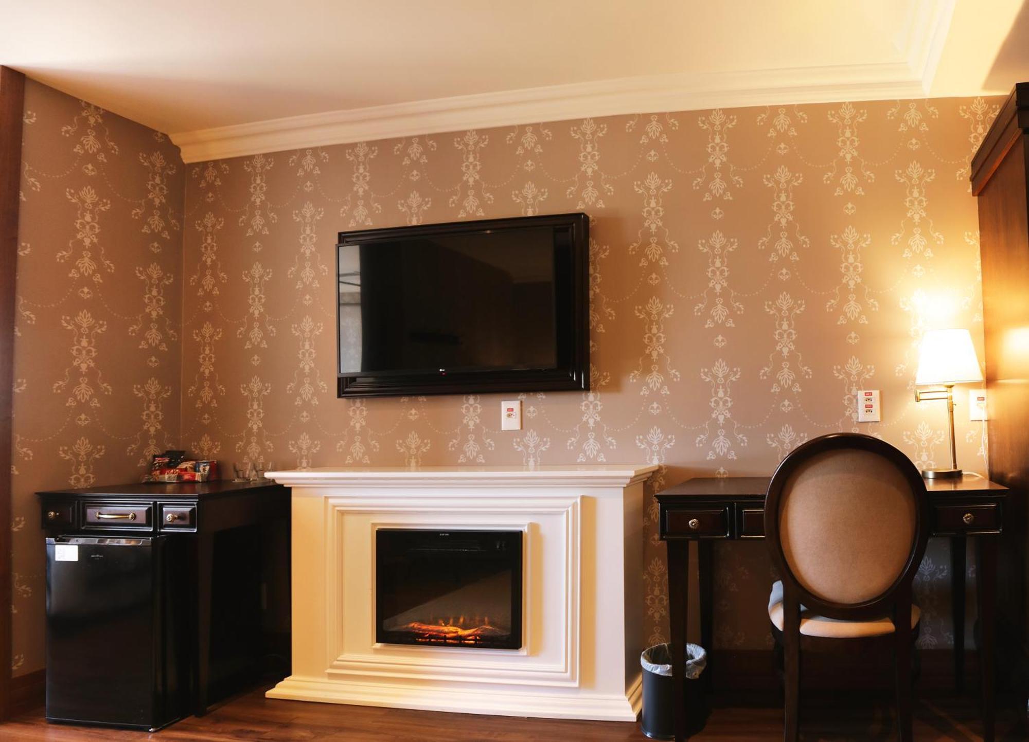 Buona Vitta Gramado Resort & Spa By Gramado Parks Екстериор снимка The photo shows a cozy room featuring a decorative wall with a subtle pattern. On one side, there is a modern flat-screen television mounted on the wall. Below it, there is a stylish electric fireplace framed in white. Adjacent to the fireplace is a 