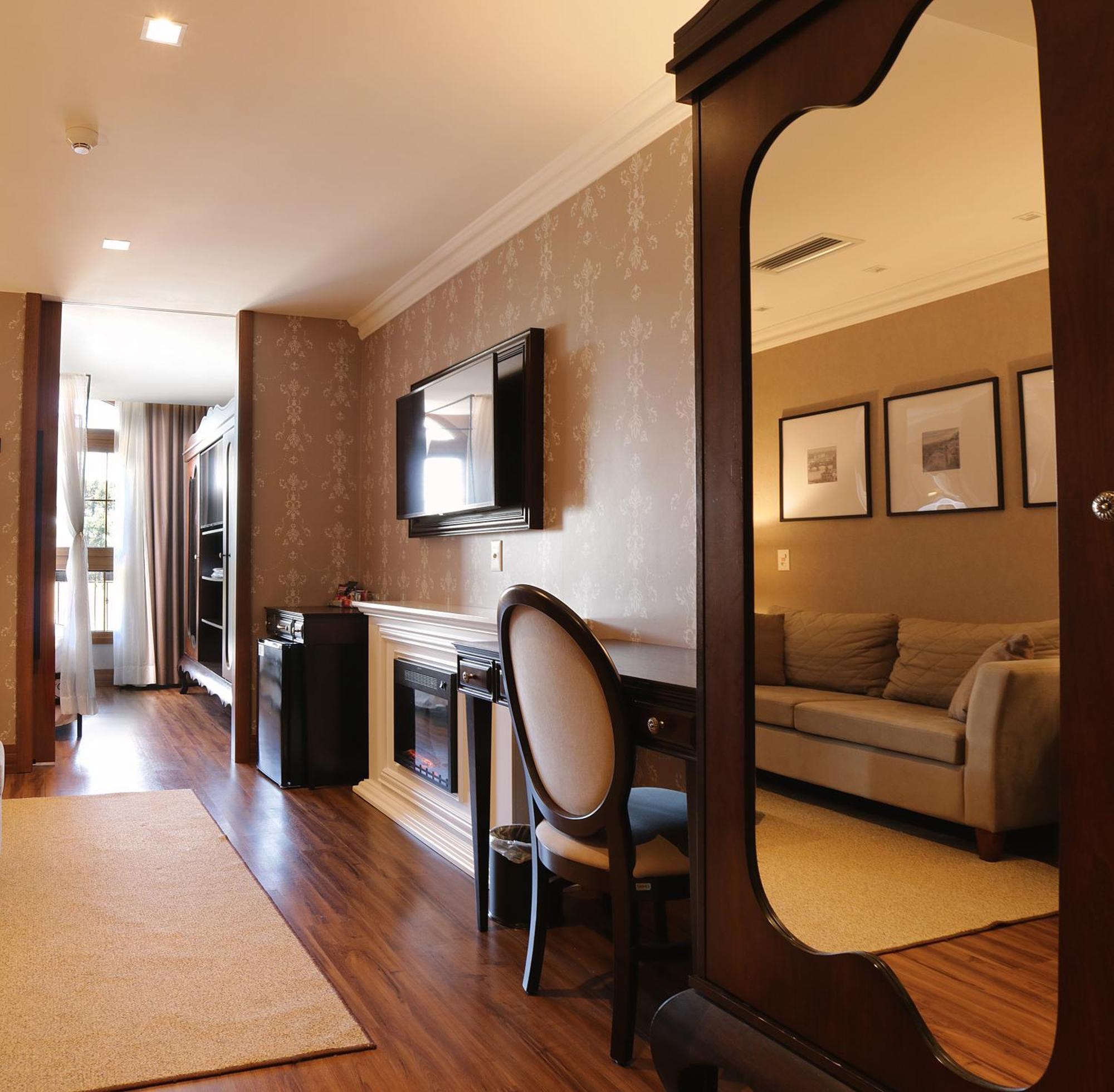 Buona Vitta Gramado Resort & Spa By Gramado Parks Екстериор снимка The photo shows a well-decorated room that appears to be a living area or a hotel suite. In the foreground, there is a round chair and a desk. A large mirror reflects the living space, creating a sense of spaciousness. 

On the wall is a flat-screen 