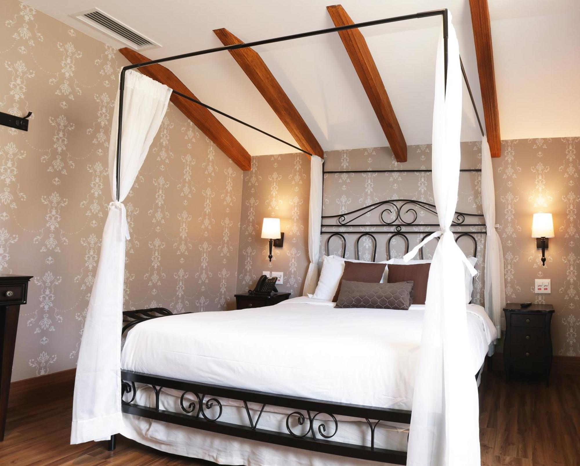 Buona Vitta Gramado Resort & Spa By Gramado Parks Екстериор снимка The photo shows a beautifully designed bedroom featuring a four-poster bed with a metal frame and flowing white curtains. The bed is adorned with white bedding and brown decorative pillows. The room has wooden beams on the ceiling and is decorated wi
