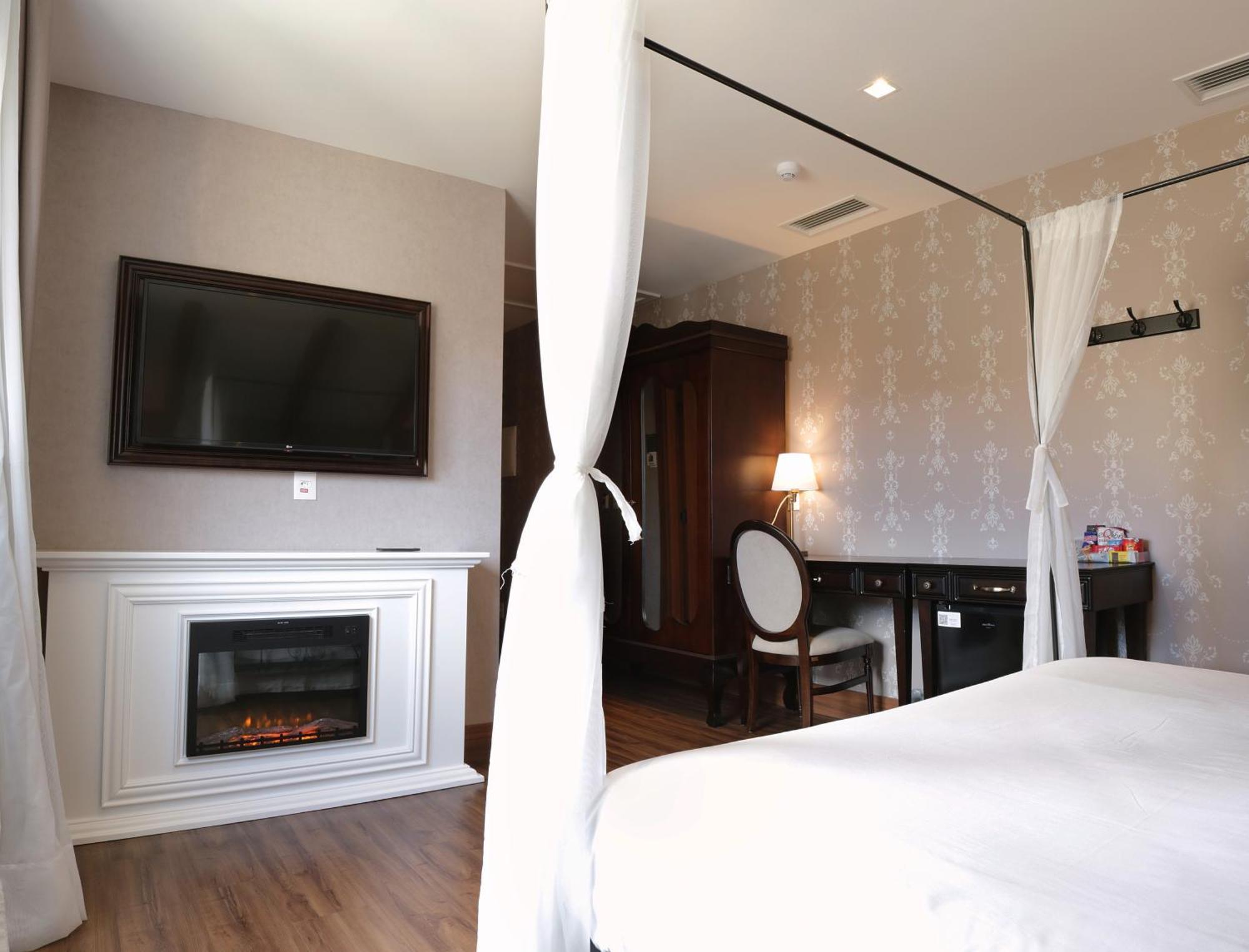 Buona Vitta Gramado Resort & Spa By Gramado Parks Екстериор снимка The photo shows a cozy hotel room with elegant decor. There is a white bed with a canopy, and a modern television mounted on the wall across from it. To the side, a fireplace is built into a white mantel, adding a warm touch to the space. There's a w