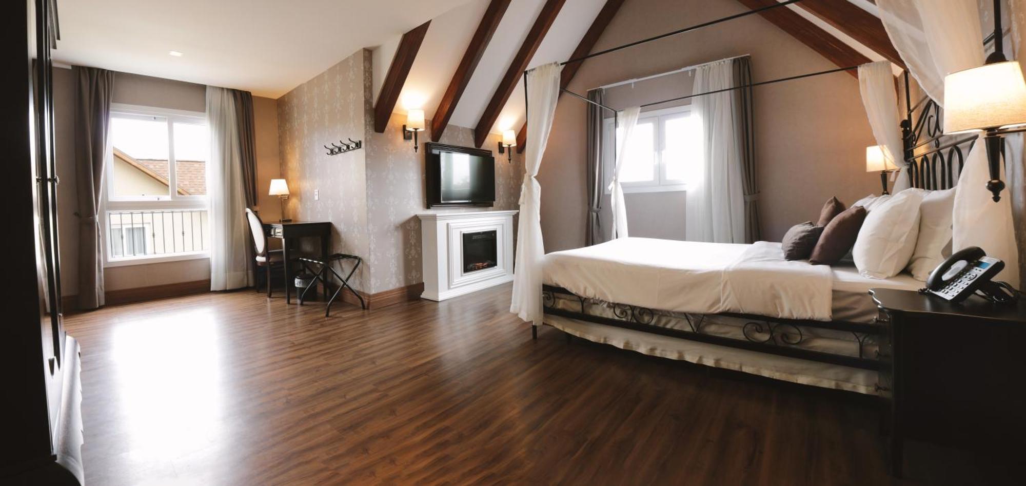 Buona Vitta Gramado Resort & Spa By Gramado Parks Екстериор снимка The photo shows a spacious hotel room with a modern and elegant design. There is a large bed with an overhead canopy, and the bed is dressed in white linens. To the side, there is a small seating area with a desk and chair. A flat-screen television i